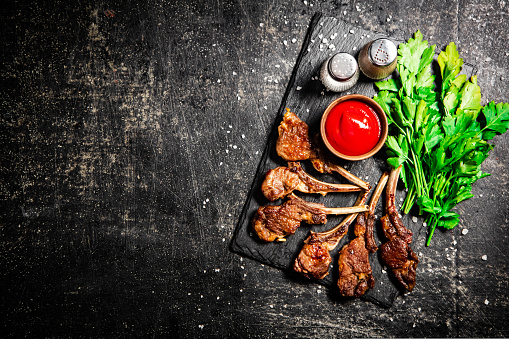 Rack of lamb with tomato sauce and parsley on the table. On a black background. High quality photo