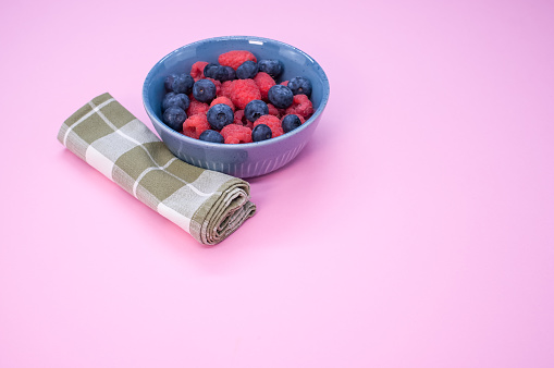 A bowl of fresh blueberries and raspberries isolated on a pink background with space for text