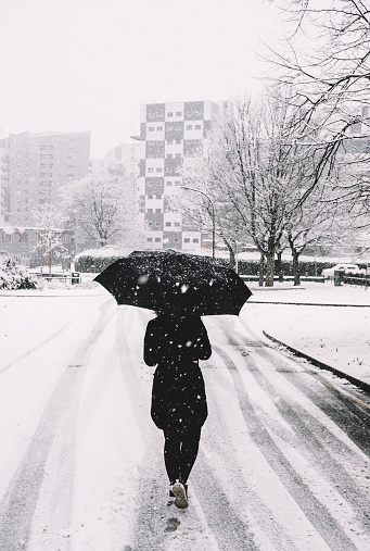 A vertical shot of a woman walks on a snowy street