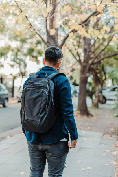 istock Back view of a young stylish male student wearing a black backpack and holding a notebook 1463722338