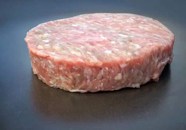 Photo of Raw beef-patty on the dark background. Close-up.