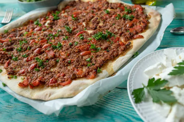 Homemade fresh baked traditional turkish pizza or lahmacun with ground beef, vegetables topping. Served with cubed feta cheese on turquoise wooden background. Closeup and front view