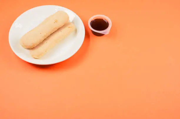 A top view of ladyfinger cookies on a plate with ketchup dip isolated on orangebackground