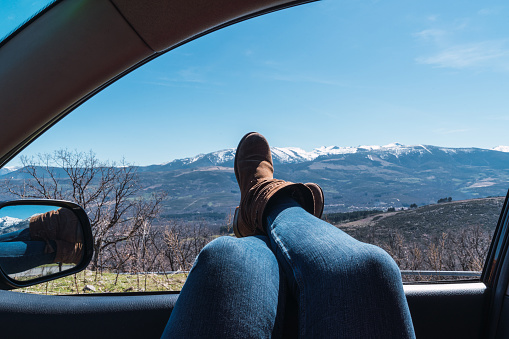 A female's feet sticking out of car window with a beautiful view of mountains under a clear sky