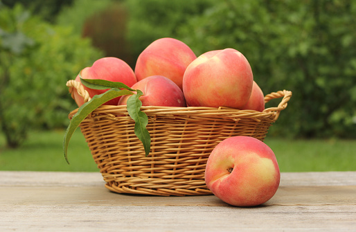 A straw basket of fresh organic peaches on the table at the farmers market