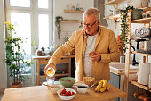 Senior man pouring water in glass while having breakfast at his domestic kitchen