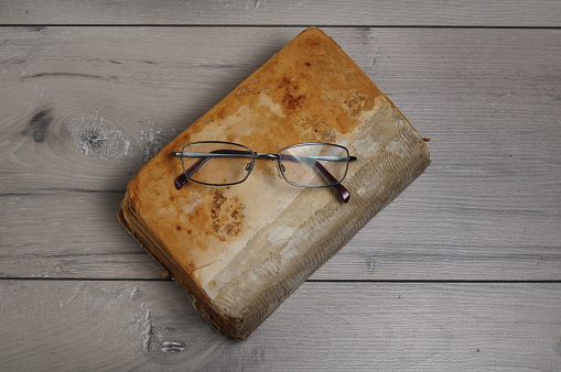 A top view of an old worn-out closed book with glasses on a wooden table