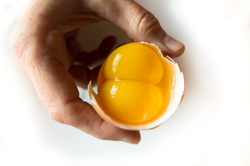 A person holding a raw egg with two yolks