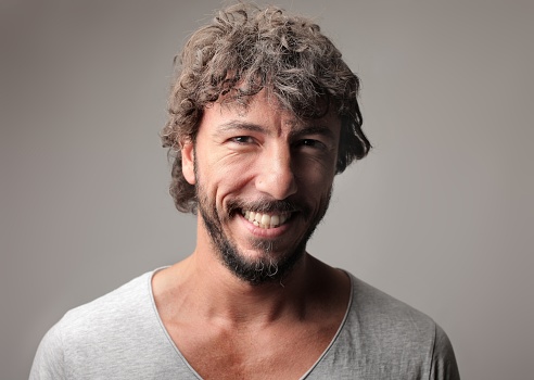 A portrait of a cheerful Italian adult man smiling against a gray background