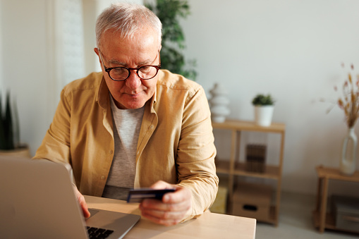 Senior man holding credit card while using laptop for online shopping