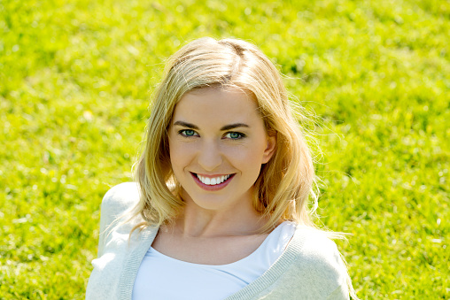 A beautiful blonde woman happily posing with green grass on the background