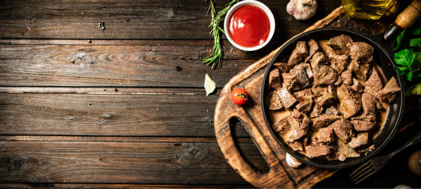Fried liver in a frying pan on a cutting board with tomato sauce.