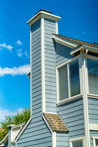 A vertical shot of a wooden house with a long chimney under a bright blue sky on a sunny day