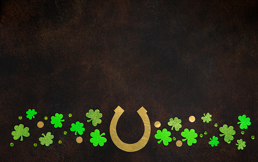St. Patrick's Day celebration Concept. Greeting card with traditional symbols - Golden horseshoe, gold coins and clover leaves, green shamrocks on dark brown wooden background. Top view, copy space.