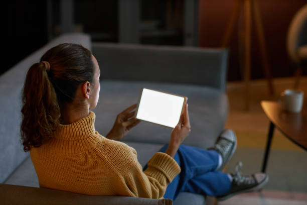 istock Woman holding digital tablet with white screen mockup relaxing on couch at home 1463776404
