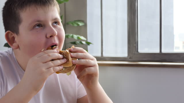 Little boy in fast food cafe eats burger. Portrait of hungry child Cute little kid eating burger. Hungry child in fast food cafe. Close-up boy eating burger. Hungry child in cafe. Lovely boy