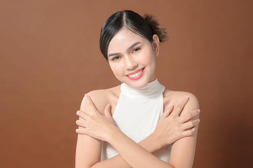 A young woman with beautiful face smiling, touching her skin over brown background , beauty skin care concept