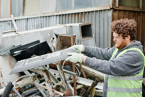 Worker putting metal piece of pile of scrap metal