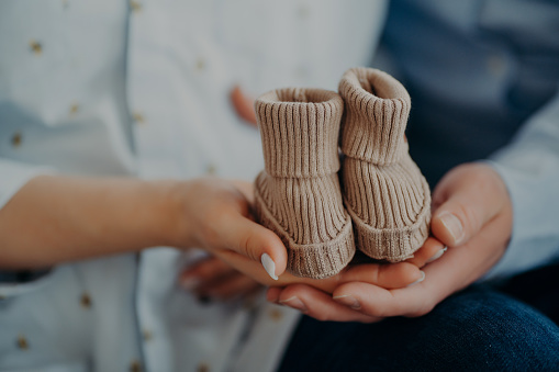 Cropped shot of future parents anticipate for child hold baby boots show small shoes for coming baby. Parenthood pregnancy birth love and family concept.