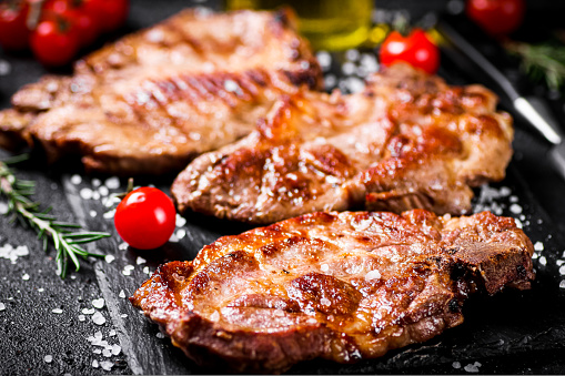 Grilled pork steak with cherry tomatoes and rosemary. On a black background. High quality photo