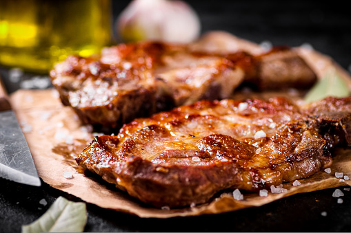 Grilled pork steak on paper on the table. On a black background. High quality photo