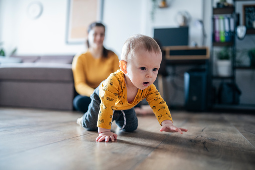 Young mother teaches her baby son to crawl at home.