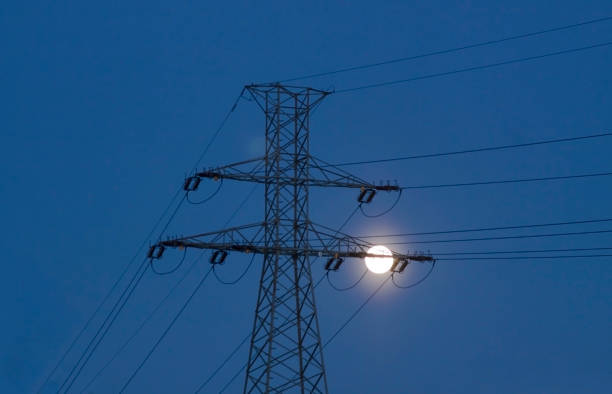 View of a high voltage line pylon, dark sky and moon in the background, symbolic image of power price crisis
