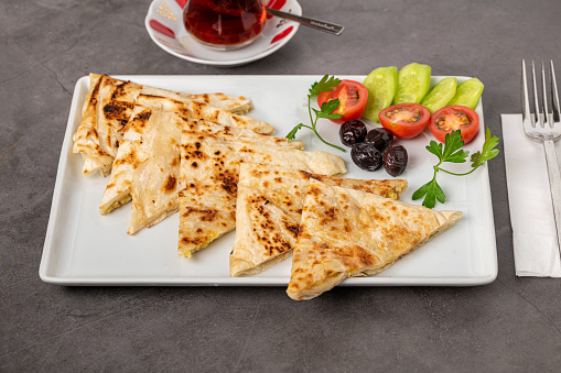 Traditional Turkish flatbread or Gozleme with tomatoes, olives and tea on dark stone table