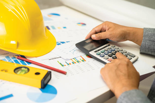 istock Asian engineer with architectural house plan project blueprint, graph and yellow helmet and engineering construction tools. 1463811855