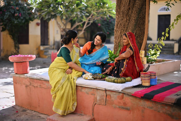 Beautiful women in saris buying glass bangles from a local Bangle Vendor sitting under a tree in a Palace in Rajasthan