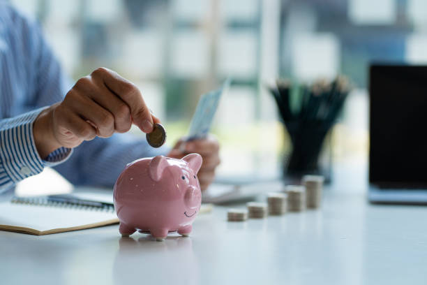 hände eines jungen asiatischen geschäftsmannes mann legt münzen ins sparschwein und hält geld nebeneinander, um ausgaben zu sparen ein sparplan, der genug von seinem einkommen für zahlungen bereitstellt. - ersparnisse stock-fotos und bilder