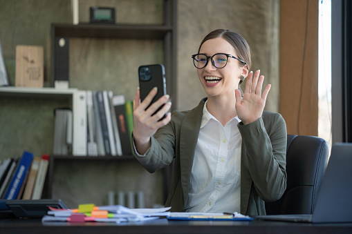 Smiling businesswoman making video calls via smartphone while sitting in the office.