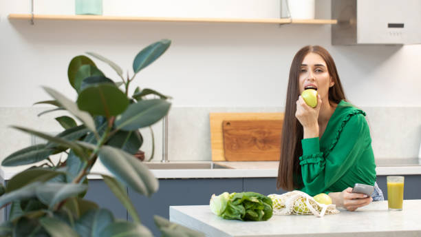 istock An attractive brunette holds a green apple while standing at the kitchen table. 1463817962