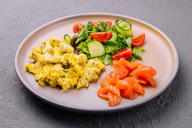 Scrambled eggs with salmon and tomato and cucumber salad stock photo