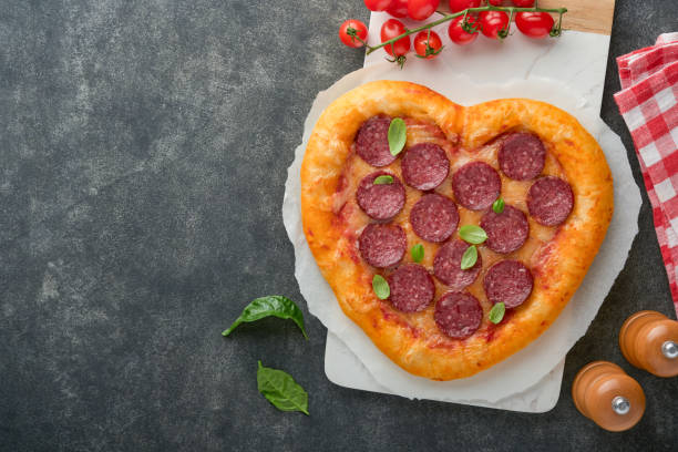 istock Valentines day heart shaped pizza with mozzarella, pepperoni and basil, wine bottle, two wineglass, gift box on black background. Idea for romantic dinner Valentines day. Top view. Mock up. 1463821161