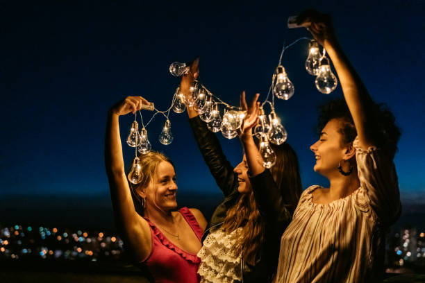 istock Three Female Friends Playing With String Lights On The Rooftop At Night 1463821229