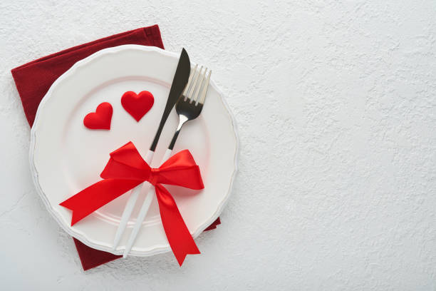 istock Valentines day romantic table setting. Empty or closeup of a dinner black plate, knife, fork and decorative silk hearts on white background. Holiday concept. Copy space for inscriptions. 1463821274