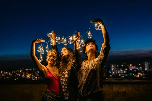 istock Three Female Friends Playing With String Lights On The Rooftop At Night 1463821356
