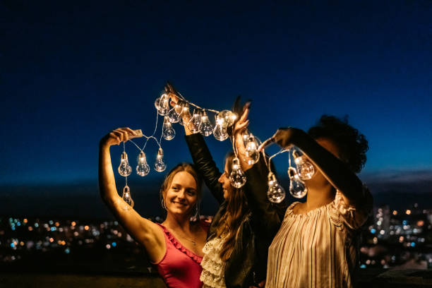 istock Three Female Friends Playing With String Lights On The Rooftop At Night 1463821541