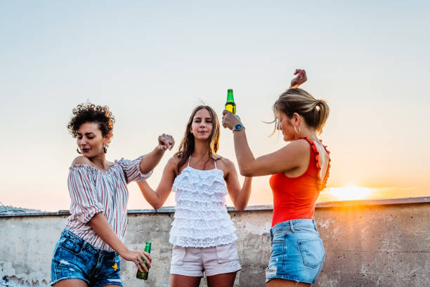 istock Three Young Female Friends Drinking Beer And Dancing On The Rooftop 1463821927