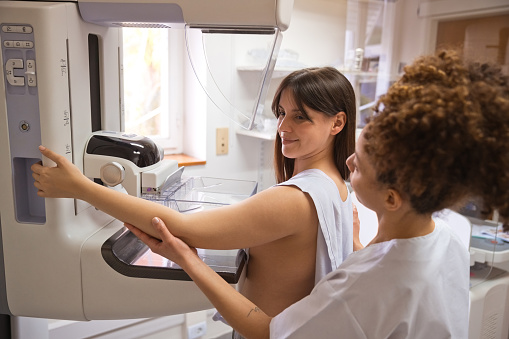 Female doctor talking to young woman during Mammography test in examination room