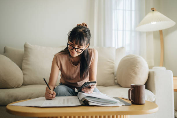 mujer asiática planificando presupuesto y usando calculadora en teléfono inteligente. - home finances fotografías e imágenes de stock