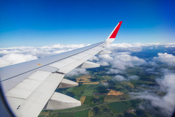 View from the airplane window on the wing to the summer green fields under the clouds. Transport and travel concept