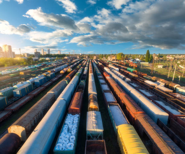 Drone view of freight trains at sunset. Colorful railway cargo wagons on railroad. Aerial view of colorful wagons, city, blue sky with clouds. Depot of freight trains. Railway station. Transportation stock photo