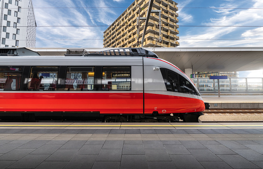 High speed train on the train station at sunset in Vienna, Austria. Beautiful red modern intercity passenger train on the railway platform, buildings. Side view. Railroad. Commercial transportation