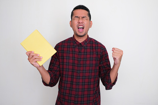 Adult Asian man screaming desperate while holding a book