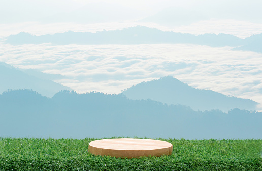 Wood podium table top on fresh green grass with outdoor mountains scene nature landscape at sunrise blur background.Natural beauty cosmetic or healthy product placement presentation pedestal display.