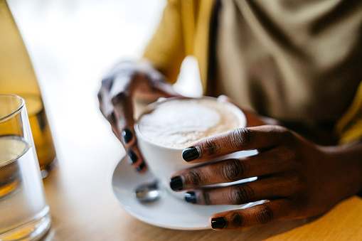 Close-up of a young black woman holding a cup of coffee in a cafe.