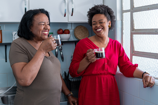 Hija y madre anciana toman café y sonríen en la cocina de casa photo