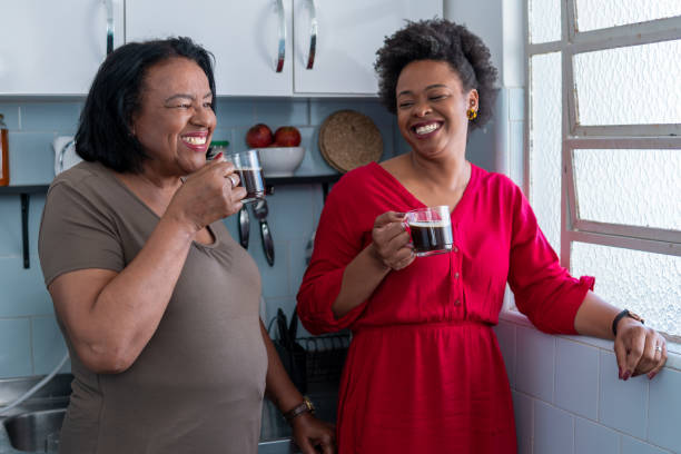 娘と年配の母親は、自宅の台所でコーヒーを飲み、笑顔で - brazilian ストックフォトと画像